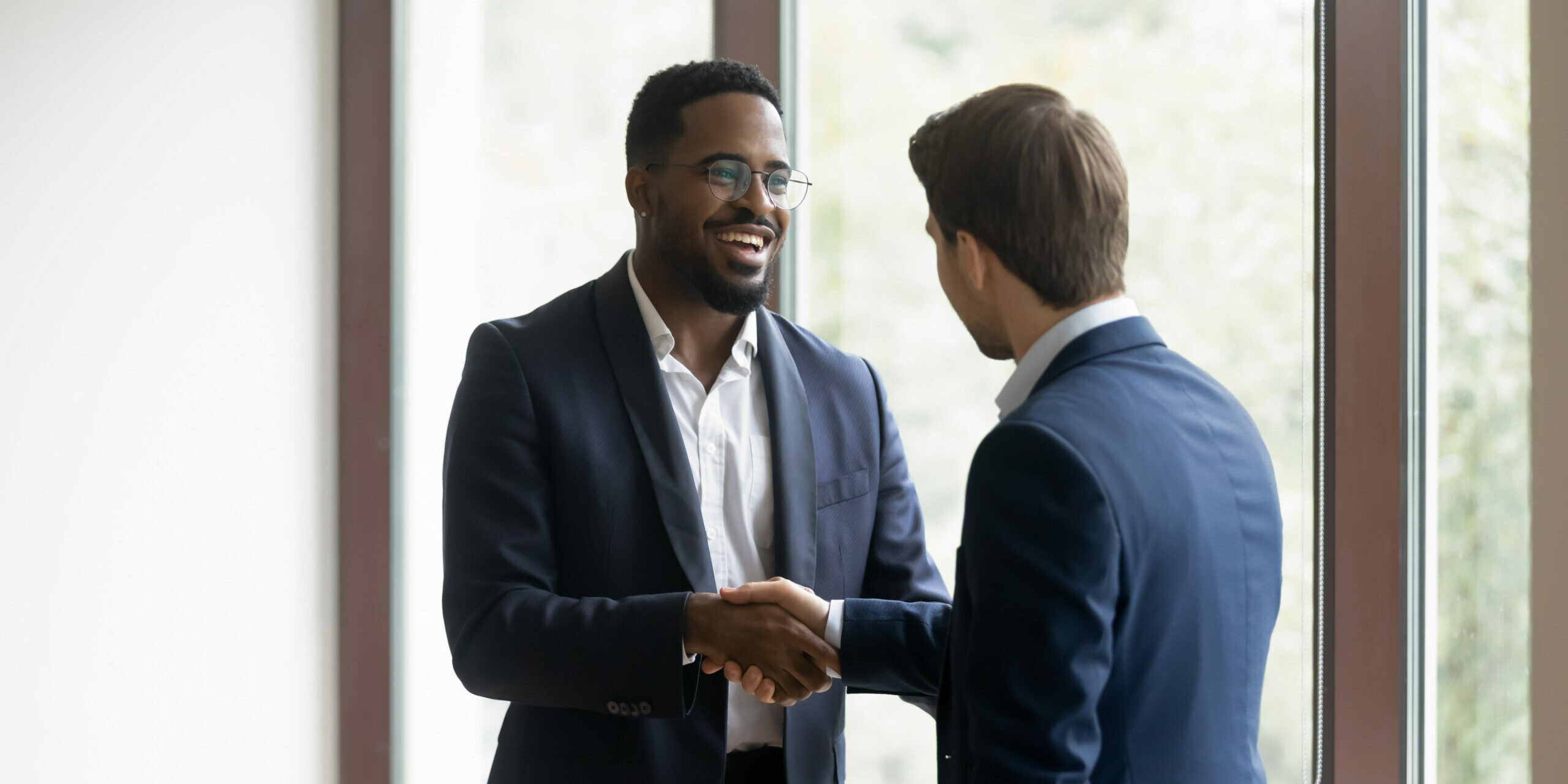 Overjoyed multiethnic businessmen shake hands greeting getting acquainted in office, smiling diverse multiracial male business partners handshake close deal make agreement after successful negotiation