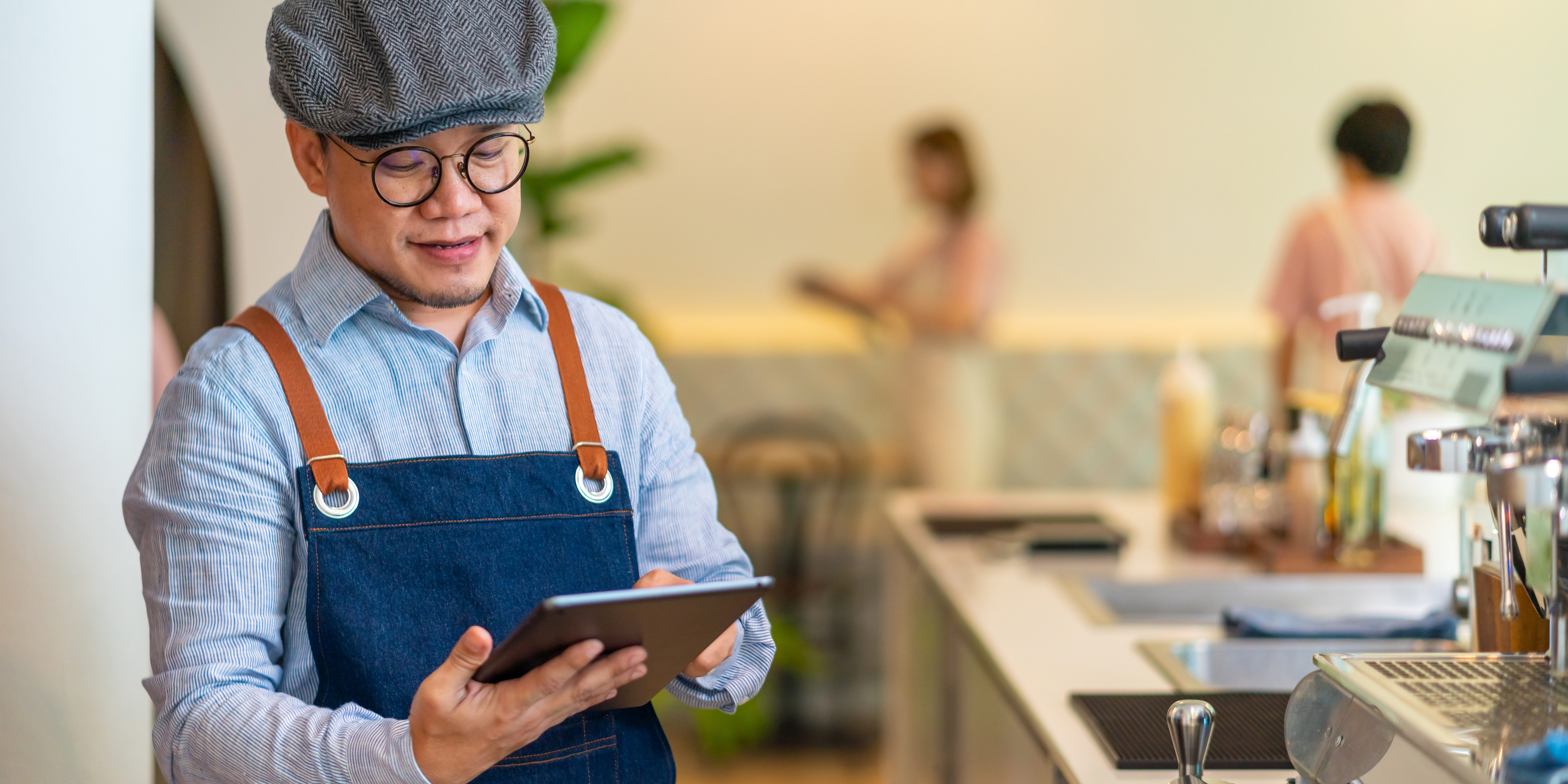 Asian man coffee shop manager walking behind bar counter working on digital tablet checking and counting inventory for ordering product for cafe. Small business restaurant owner entrepreneur concept