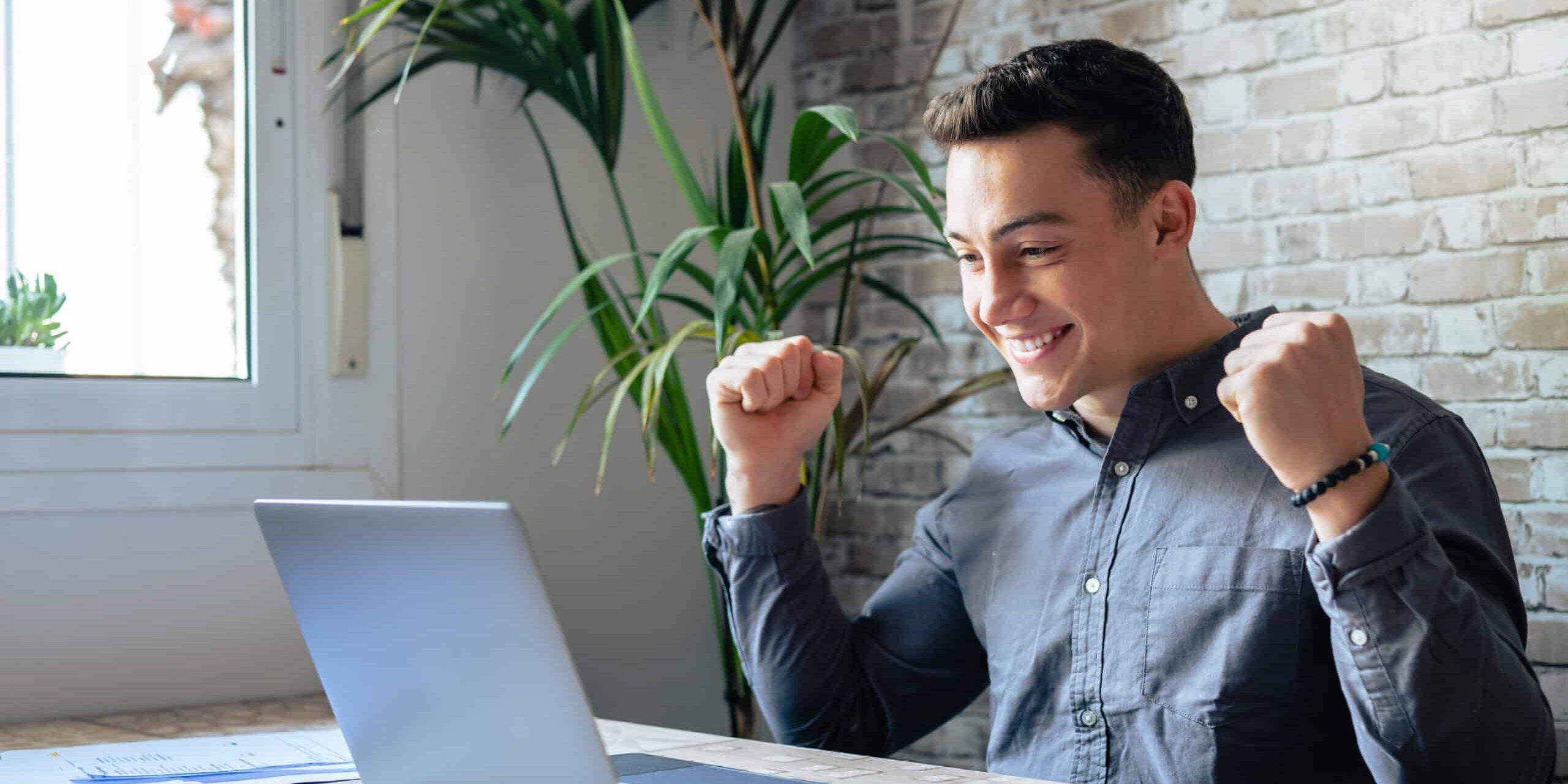 Man sit at desk read e-mail on laptop makes yes gesture feels happy. Male entrepreneur get great business news, celebrate career growth, advance. Achievement, win, moment of auction victory concept